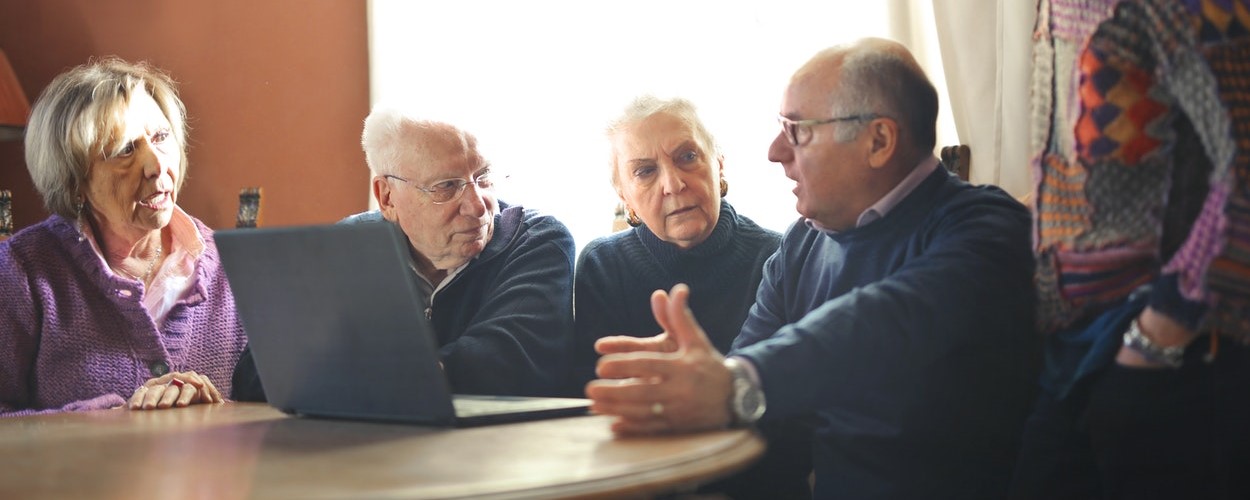 A group of four older people sitting around a table with a laptop.